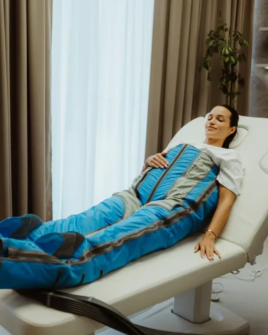 A model reclines on a treatment lounger in a blue BallancerPro compression suit over her legs, hips and abdomen