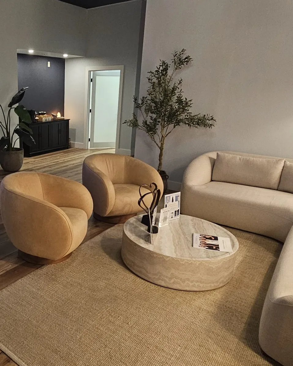 Guest lounge at Eternal MedSpa Sarasota: tan swivel chairs, a round travertine table and a curved cream sofa