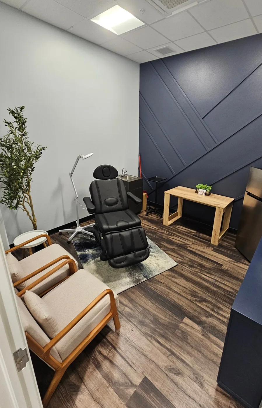 Treatment room at Eternal MedSpa Venice, with a black treatment chair, an exam lamp, a small desk and two armchairs